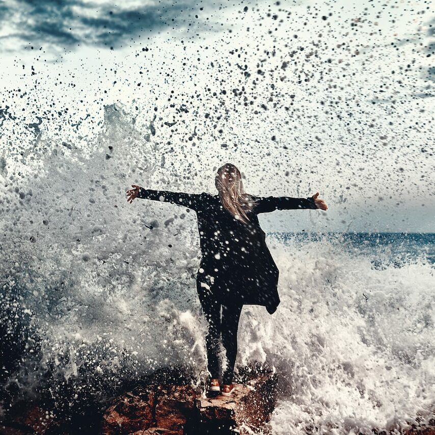 photo of woman with arms raised in the splashing waves, looking at view and getting away from it all.